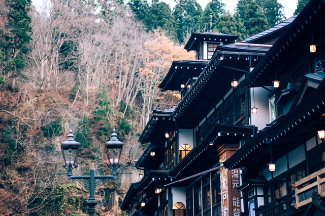 Traditional Japanese wooden building with decorative lanterns, surrounded by trees in autumn foliage.