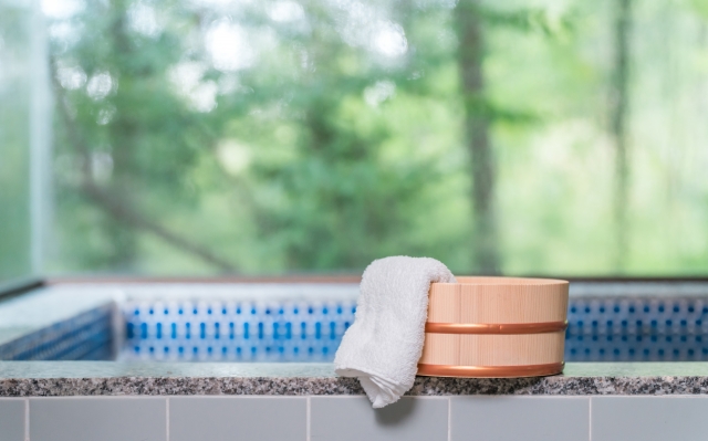 A wooden bath bucket with a white towel resting on the edge, beside a pool, with green foliage in the background.