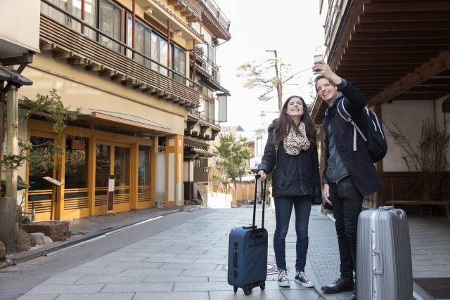 A young couple taking a selfie on a peaceful street while holding luggage, surrounded by traditional buildings.