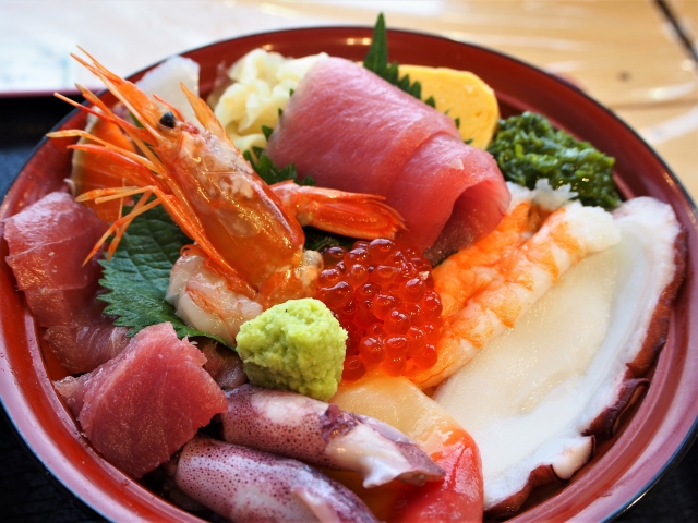 A colorful bowl of sashimi featuring various seafood including tuna, shrimp, salmon roe, and squid, garnished with wasabi and vegetables.